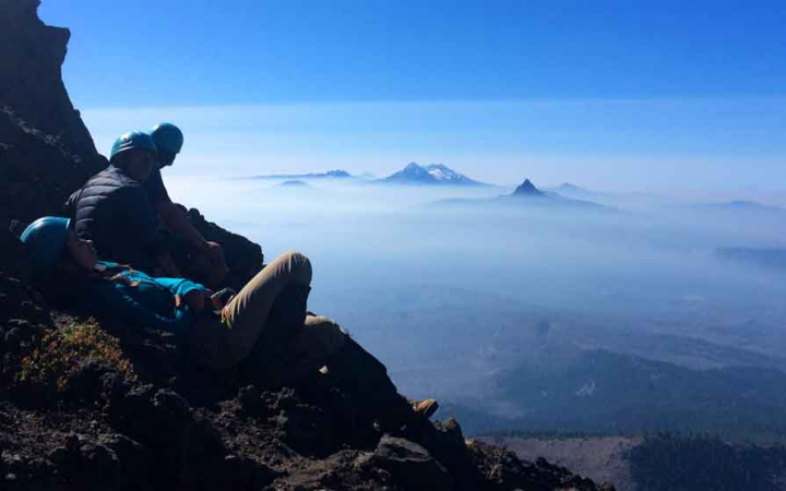students rest on rocks high above the clouds while observing mountain peaks in the distance